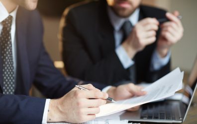 Closeup portrait of two unrecognizable  business partners reviewing paperwork and signing contract papers at table during meeting